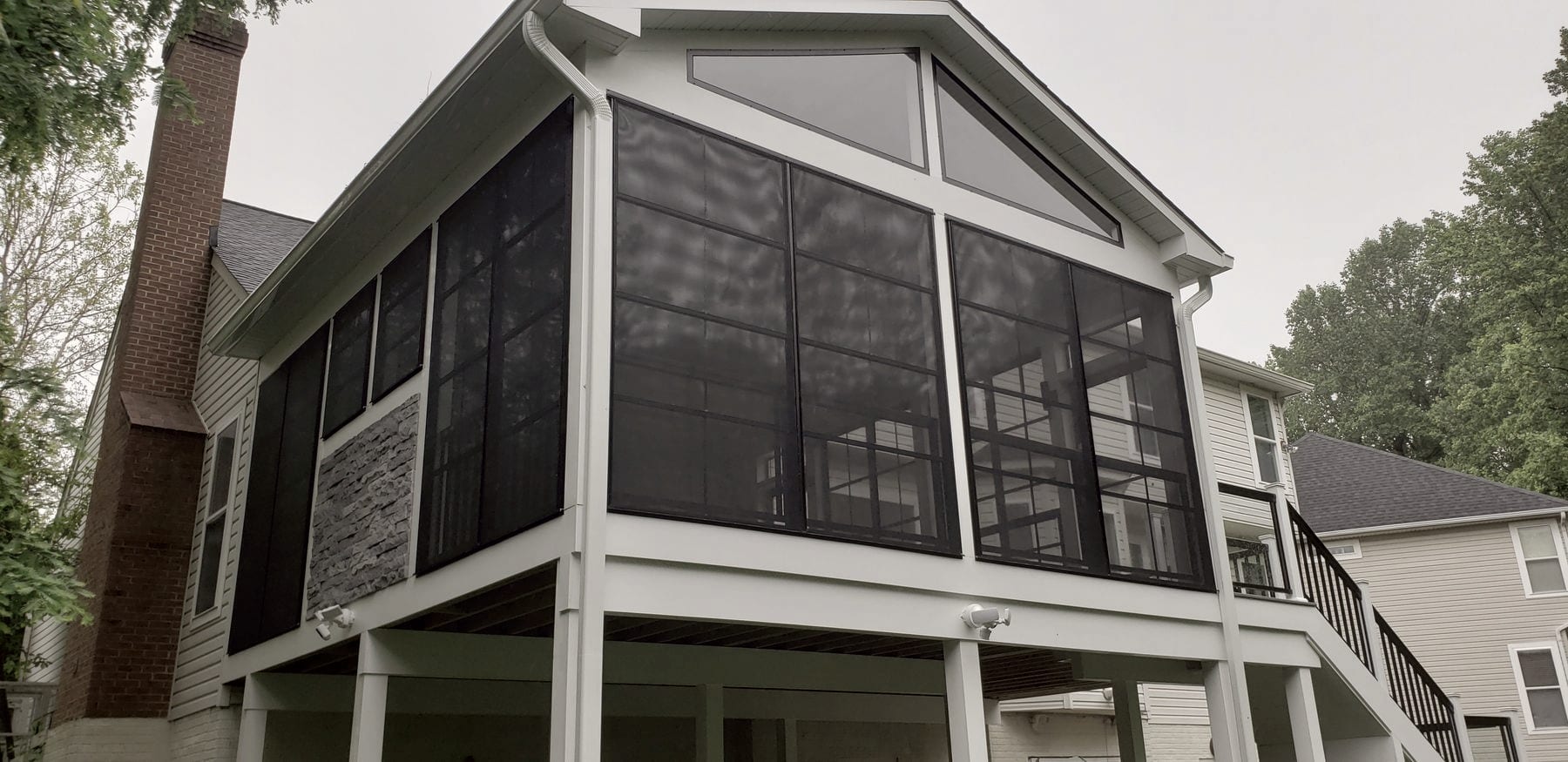 An elevated screened porch addition with a gable roof and stone accent