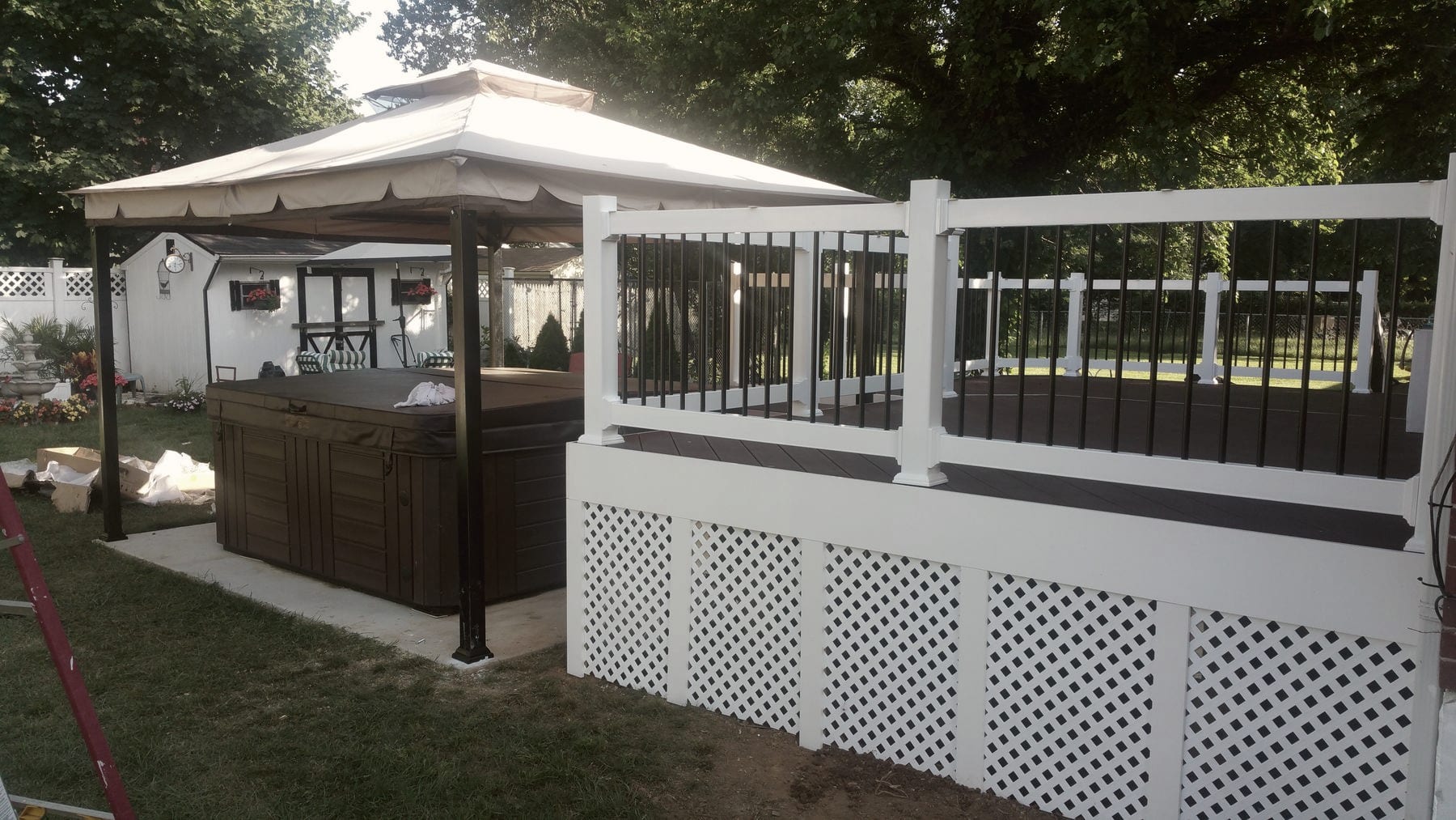 A deck with a pergola and a hot tub behind white lattice